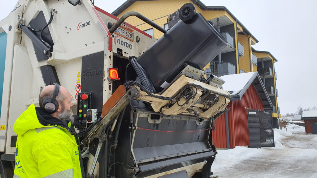 Punnitseva jäteauto tyhjentämässä jäteastiaa, kuljettaja käyttää laitteistoa auton vieressä.