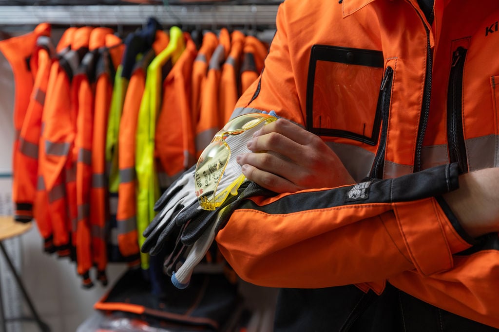 lähikuva työhanskoista ja turvalaseista ihmisen olkavarren päällä.