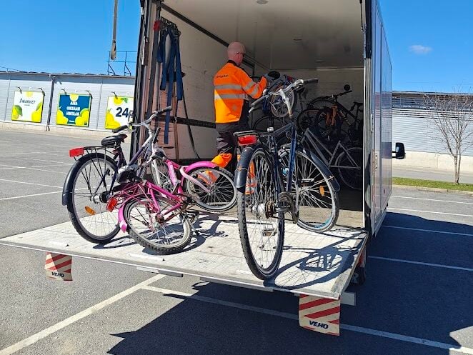 Työntekijä järjestelee polkupyöriä kuorma-autoon aurinkoisena kevätpäivänä kaupan parkkipaikalla.