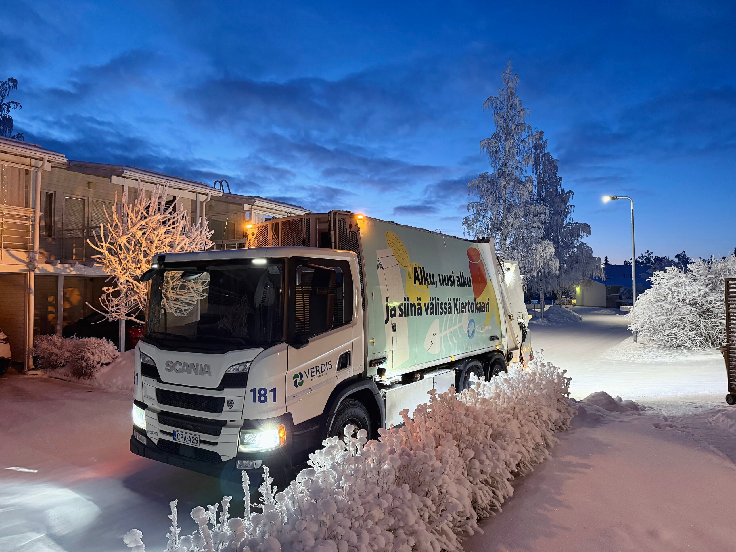 Kiertokaaren jäteauto rivitalon pihalla lumisessa maisemassa.